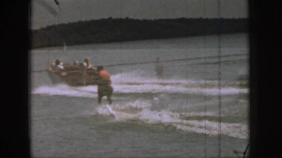 1961 Michigan home-movie frame with a motorboat, several passengers, and a water skier following through the wake on a lake.