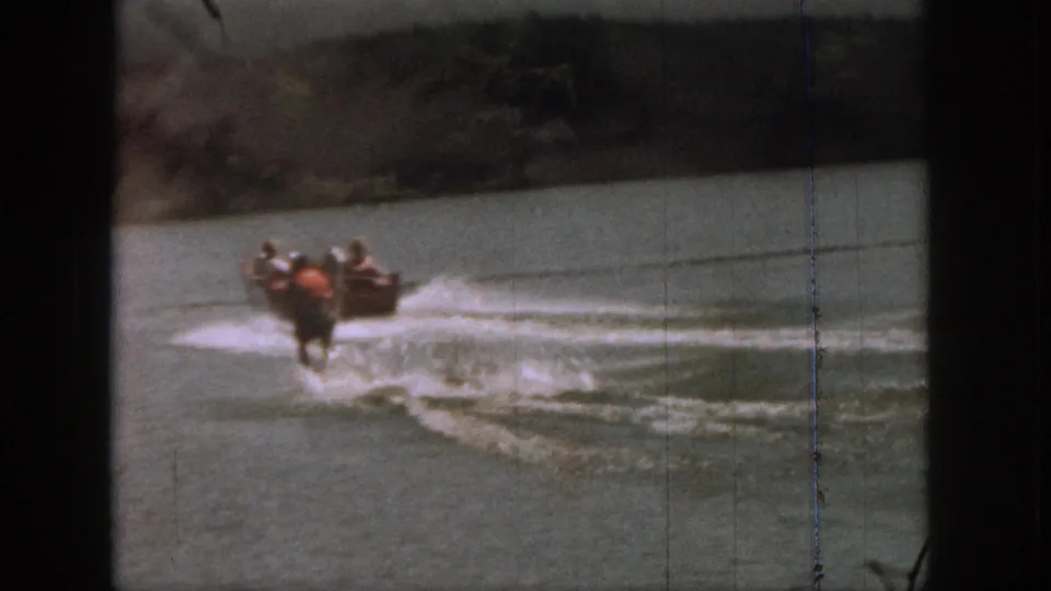 1961 Michigan 8mm frame showing a small motorboat and distant water skier moving away across the lake surface.