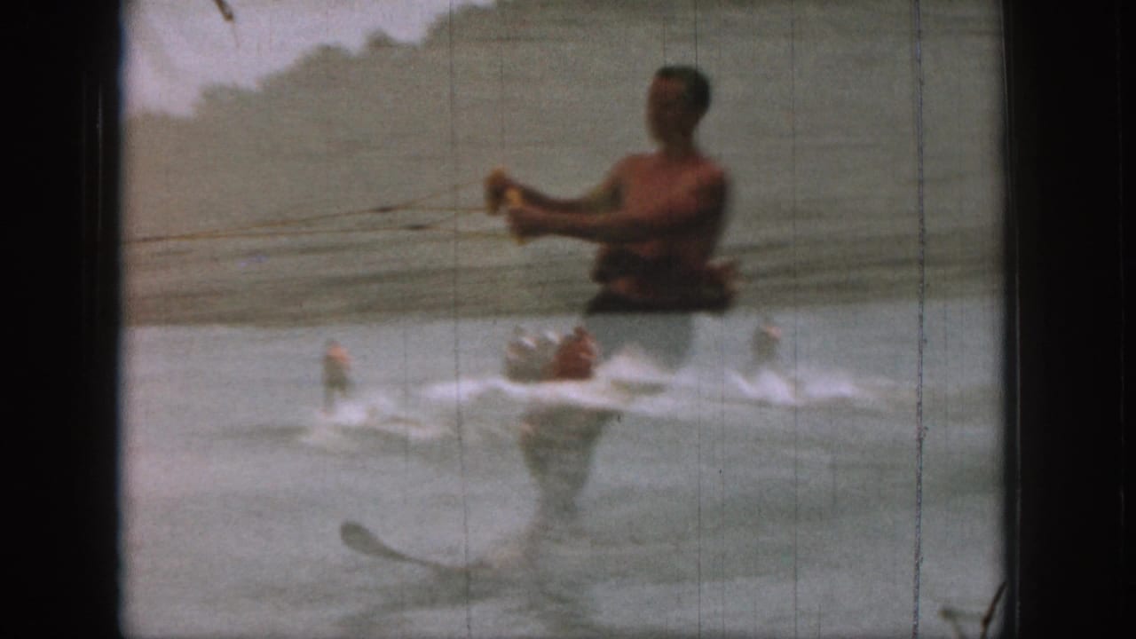 Water skier holds a tow rope near a boat on a lake, with a larger figure partly overlaid by exposure.