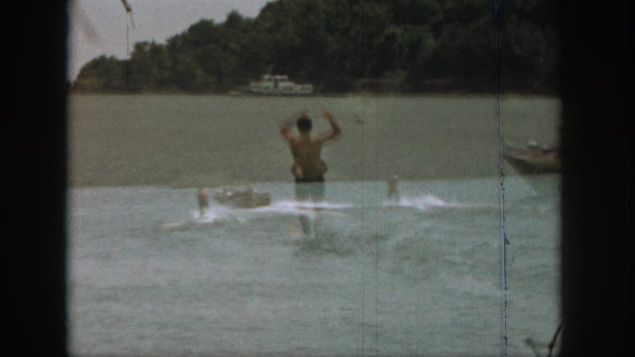 Shirtless water skier on a lake with arms raised and wakes behind him.