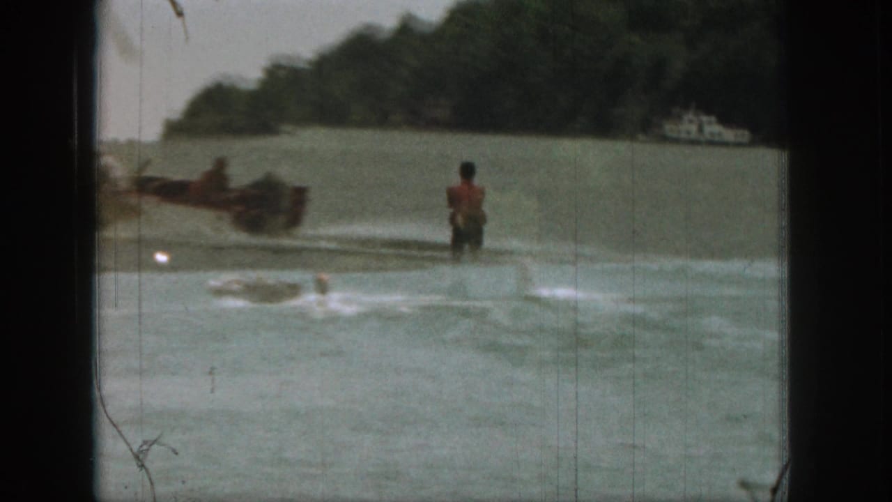 1961 Michigan 8mm frame with a motorboat towing a water skier across calm lake water near trees.