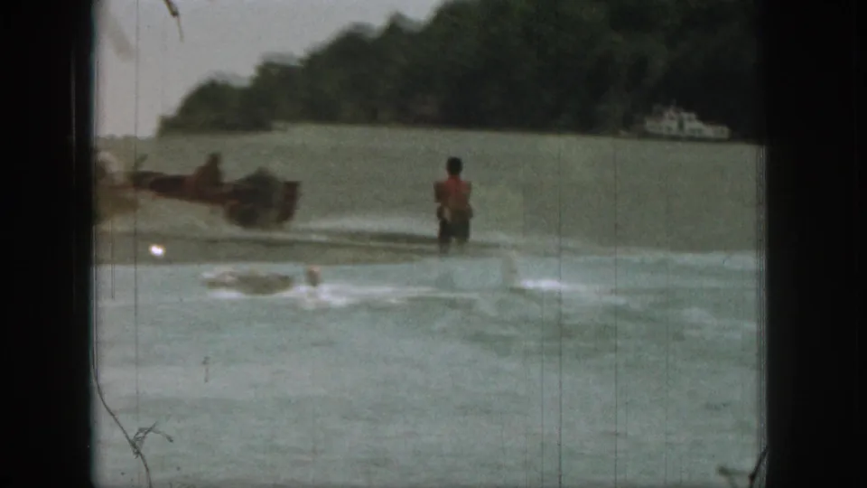 1961 Michigan 8mm frame with a motorboat towing a water skier across calm lake water near trees.