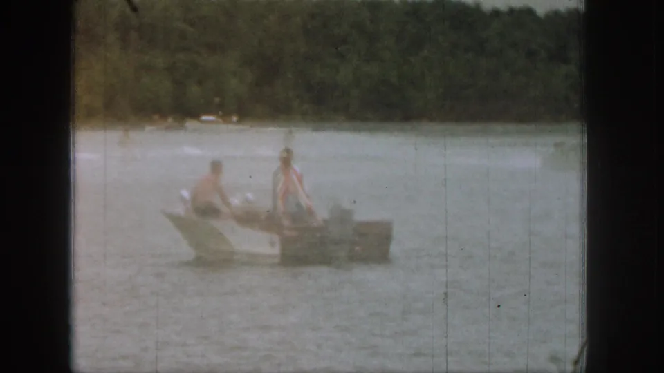 1961 Michigan 8mm frame showing two people in a small boat on a lake, with wooded shoreline in the background.