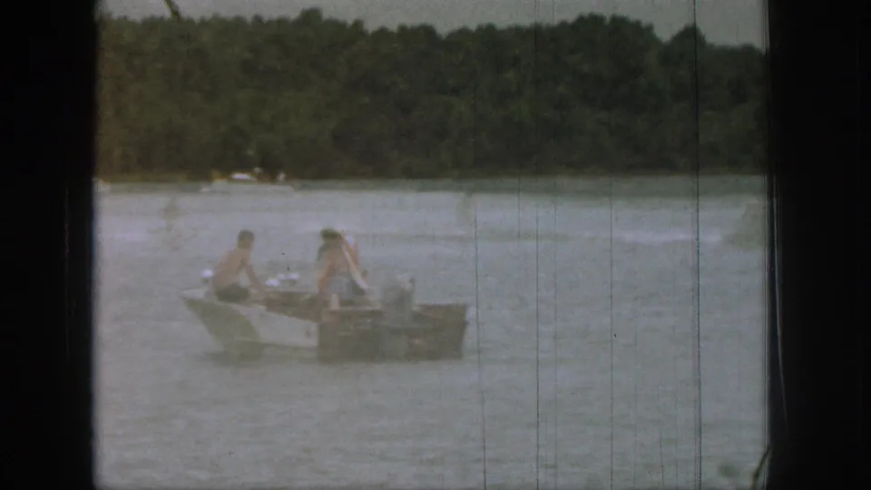 1961 Michigan 8mm frame showing a small boat with two people aboard on a calm lake bordered by trees.