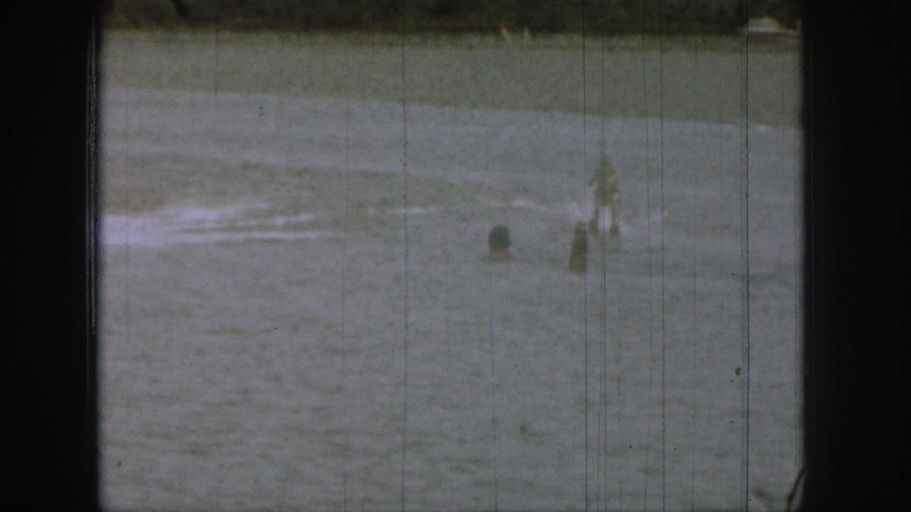 1961 Michigan 8mm frame showing swimmers spread across a lake with wake on the water and a low shoreline in the background.