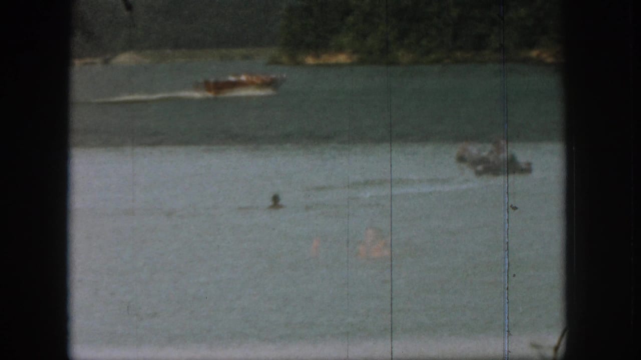 A motorboat speeds across the lake as swimmers appear in the water.