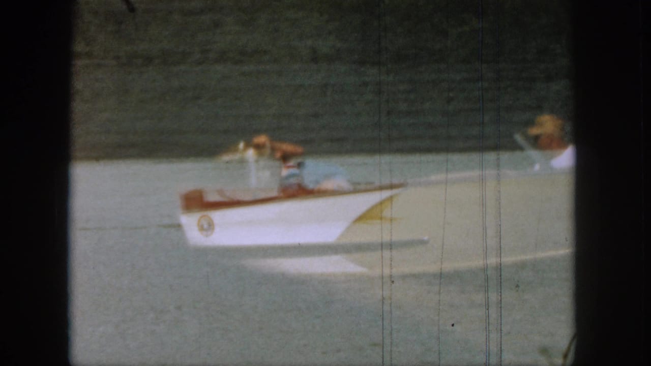 White motorboat with passengers on the lake, viewed through dark film borders.