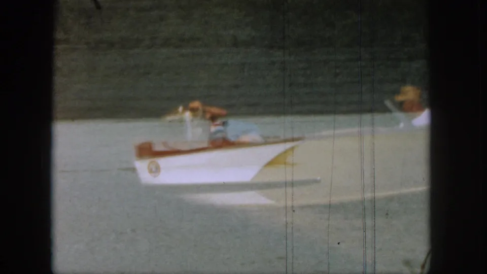 1961 Michigan lake scene with a white motorboat carrying passengers, soft focus, faded color, and visible 8mm frame borders.