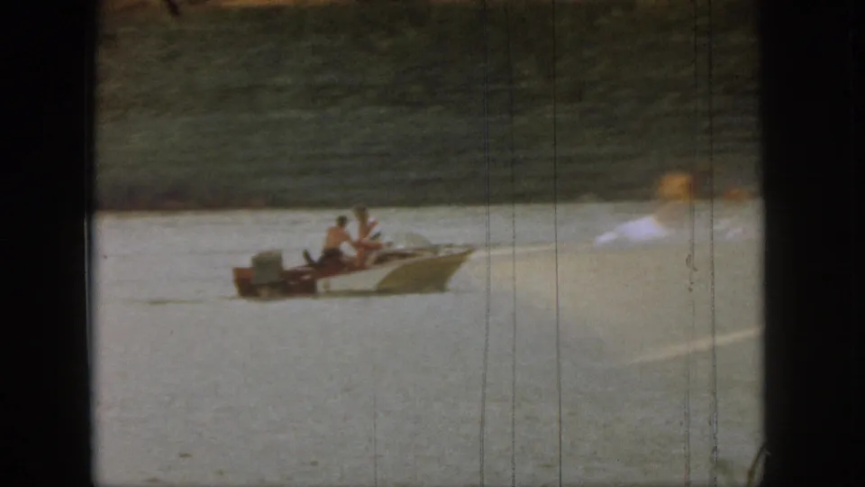 1961 Michigan 8mm frame showing a small motorboat with passengers on lake water, partly obscured by a blurred foreground figure.
