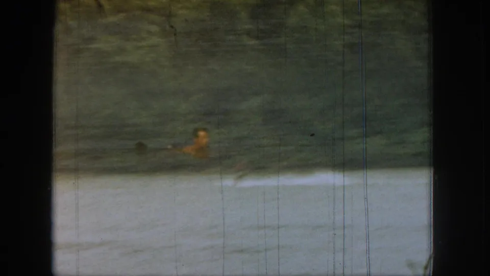 Distant water skier on a calm Michigan lake, partially framed by the boat window in 1961 home-movie footage.