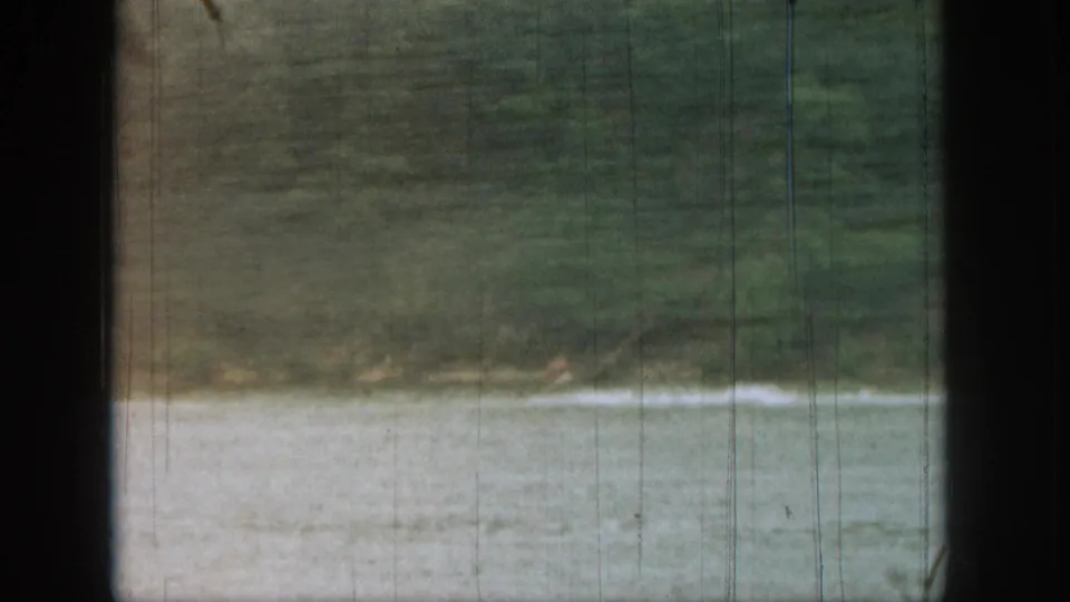A distant water skier nears the edge of frame on a Michigan lake, with wake spray and dark boat-window borders visible.