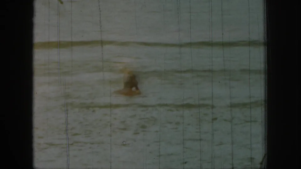 1961 Michigan 8mm frame with a partly submerged swimmer in open water, softened by faded exposure, grain, and vertical scratches.
