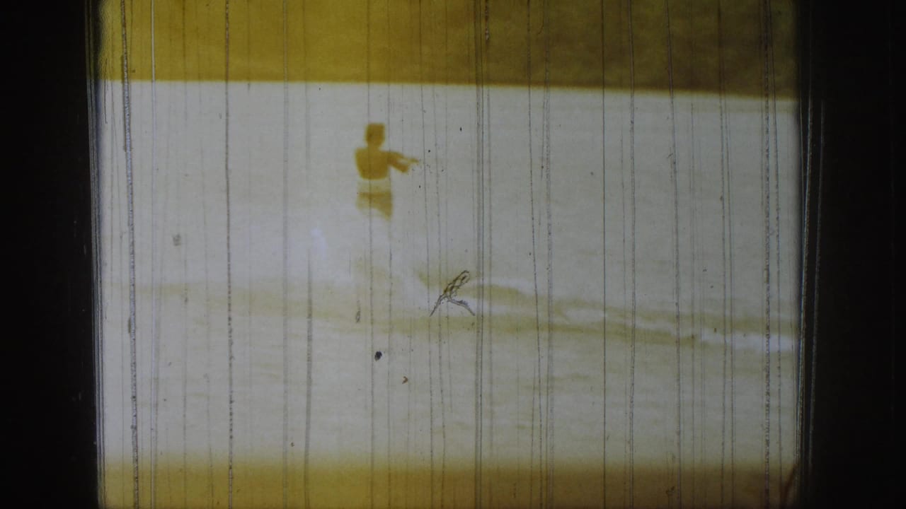 Final 1961 Michigan 8mm frame shows a distant person on lake water, pale wake lines, and pronounced vertical film wear.