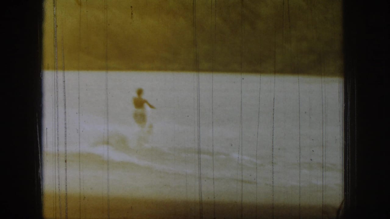 1961 Michigan 8mm frame showing a distant waterboarder on a lake, with warm fading, scratches, and dark film borders.