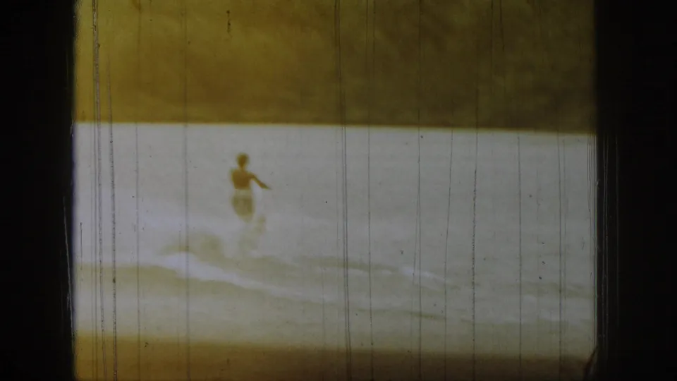 1961 Michigan 8mm frame showing a distant waterboarder on a lake, with warm fading, scratches, and dark film borders.