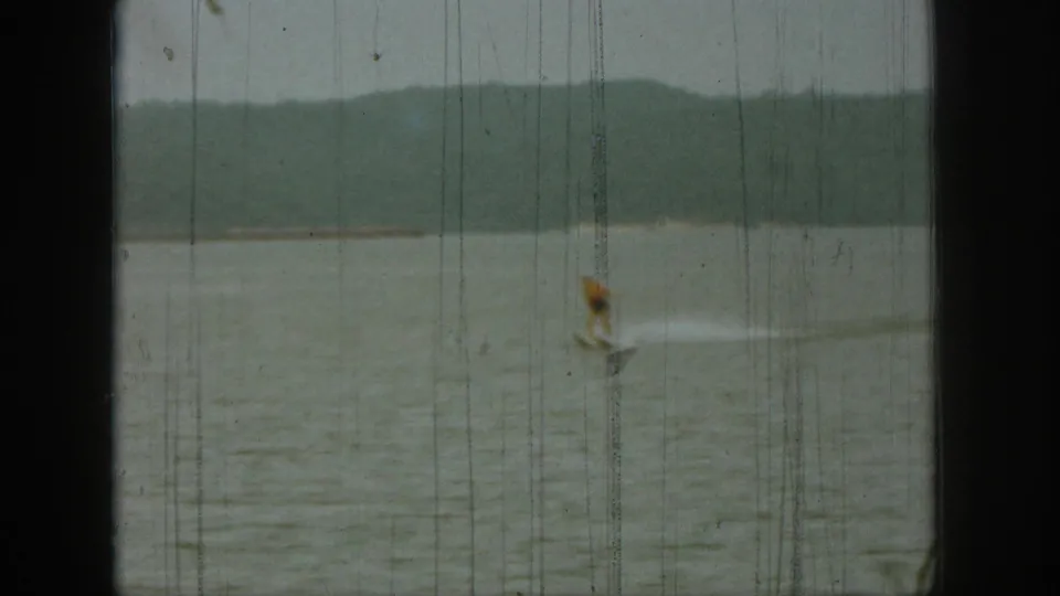 Soft 8mm frame from 1961 Michigan showing a distant figure on lake water, low hills beyond, and visible film wear.