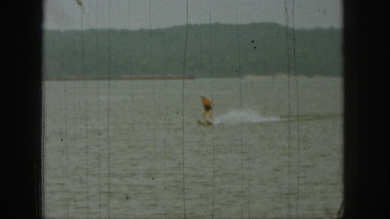 Distant water-skier crossing a lake with wooded shoreline behind.