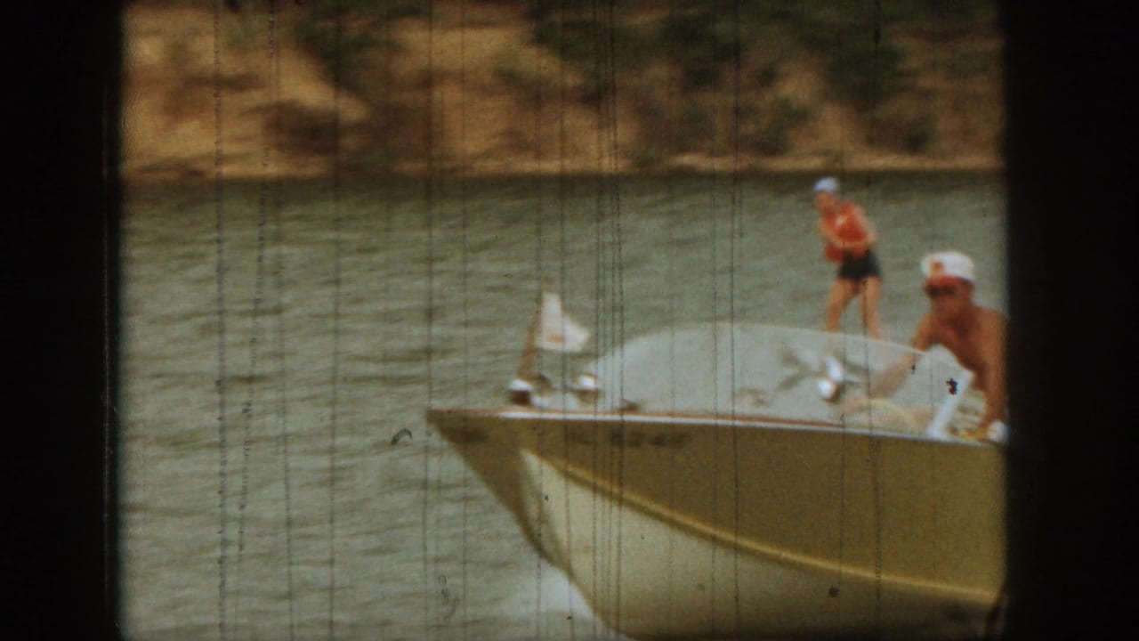 Boat on the lake with a woman water skiing behind it near a tree-lined shore.