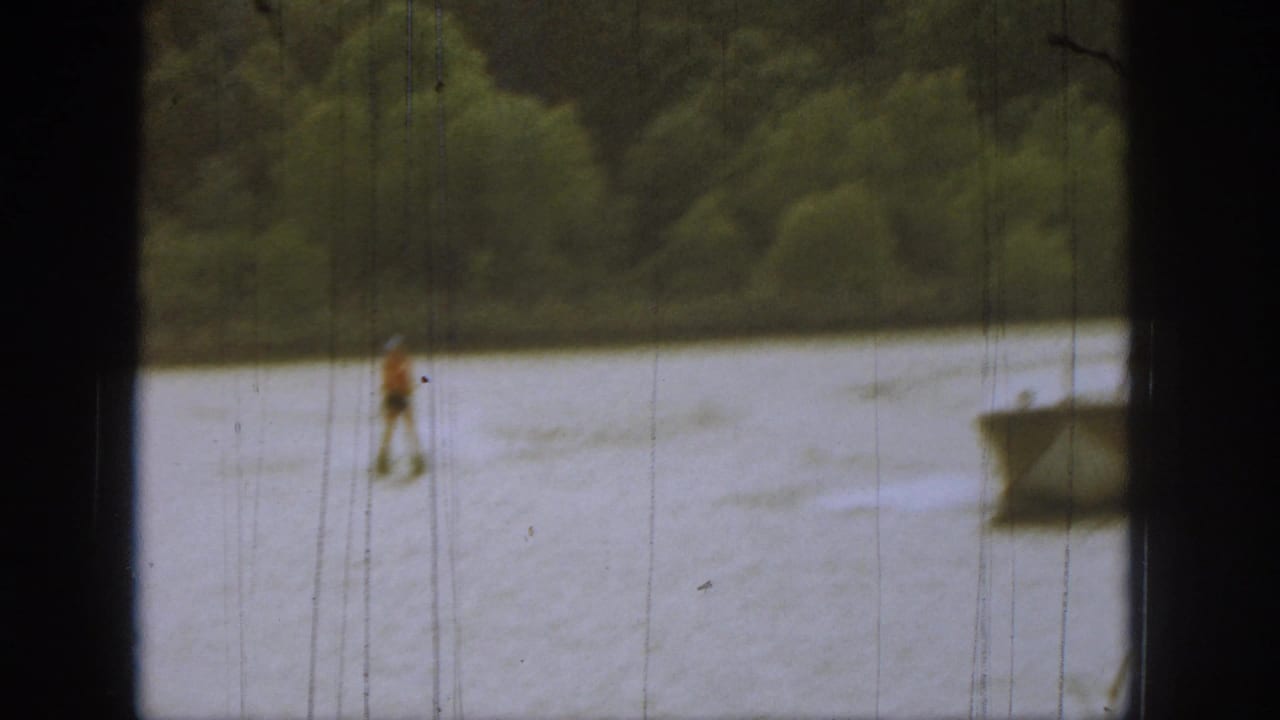 Distant water skier moves across the lake with wooded shoreline behind.