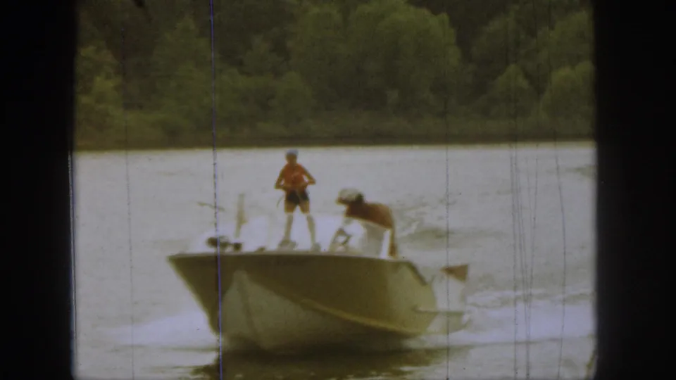 1961 Michigan lake frame showing a small motorboat with two visible people as the skier and wake pass nearby.