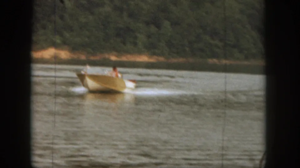 A small motorboat pulls a water skier across a Michigan lake, captured in soft 1961 8mm home-movie footage.