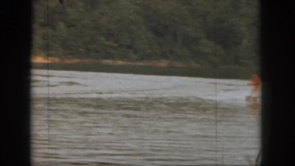 The water skier appears near the right edge of the 1961 Michigan lake scene, with wake lines spreading across the water.
