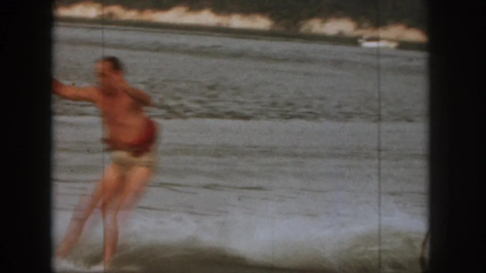 Adult man in swim trunks appears off balance in the water during a 1961 Michigan lake recreation scene.