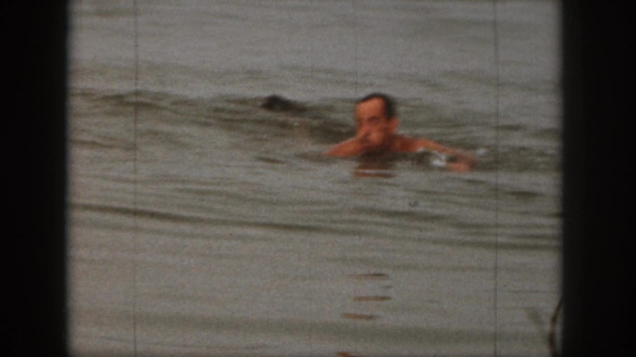 Adult man swims through the lake after the waterski fall, filmed in soft-focus 8mm home-movie style in Michigan in 1961.