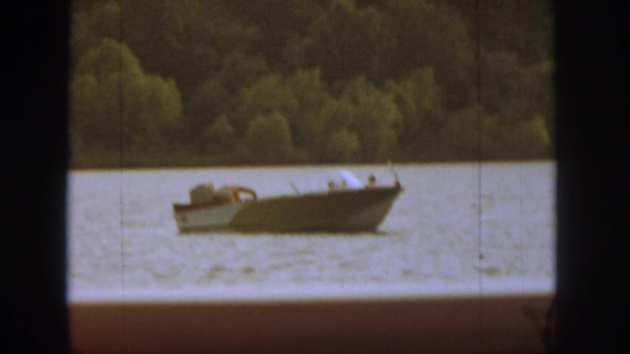 Small motorboat on a river seen through dark window framing with trees behind it.
