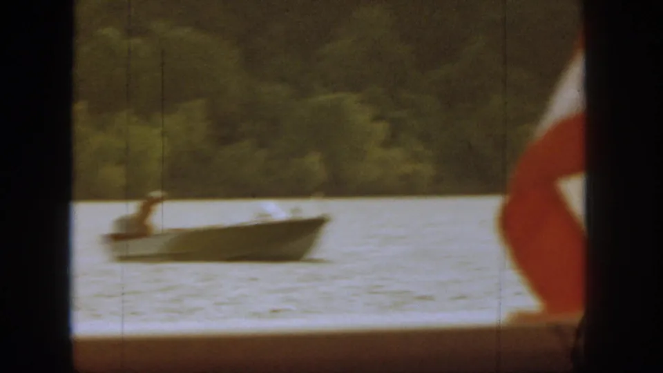 Small motorboat on Michigan river water with trees beyond and a red-and-white flag-like shape near the foreground edge.