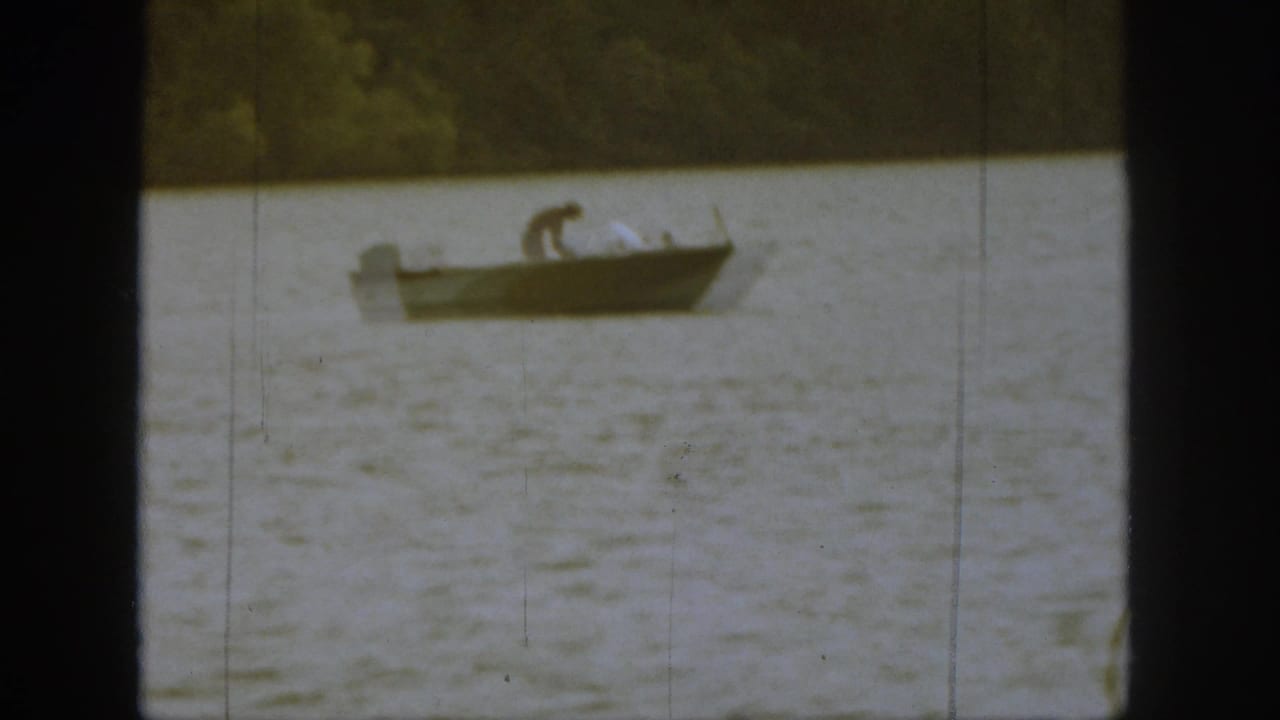 Small boat on a lake with a man bending near the center.