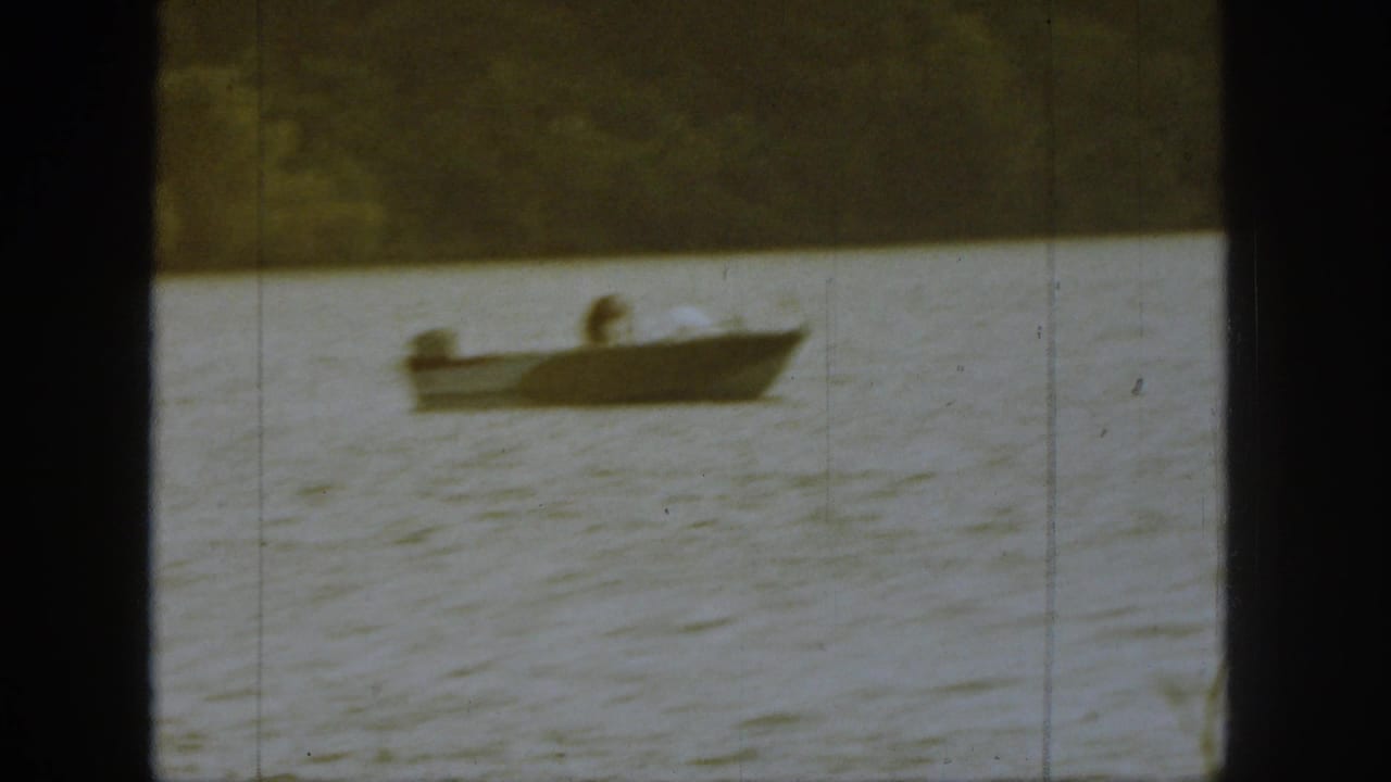 Small boat floating on the lake with a seated or bent figure aboard.