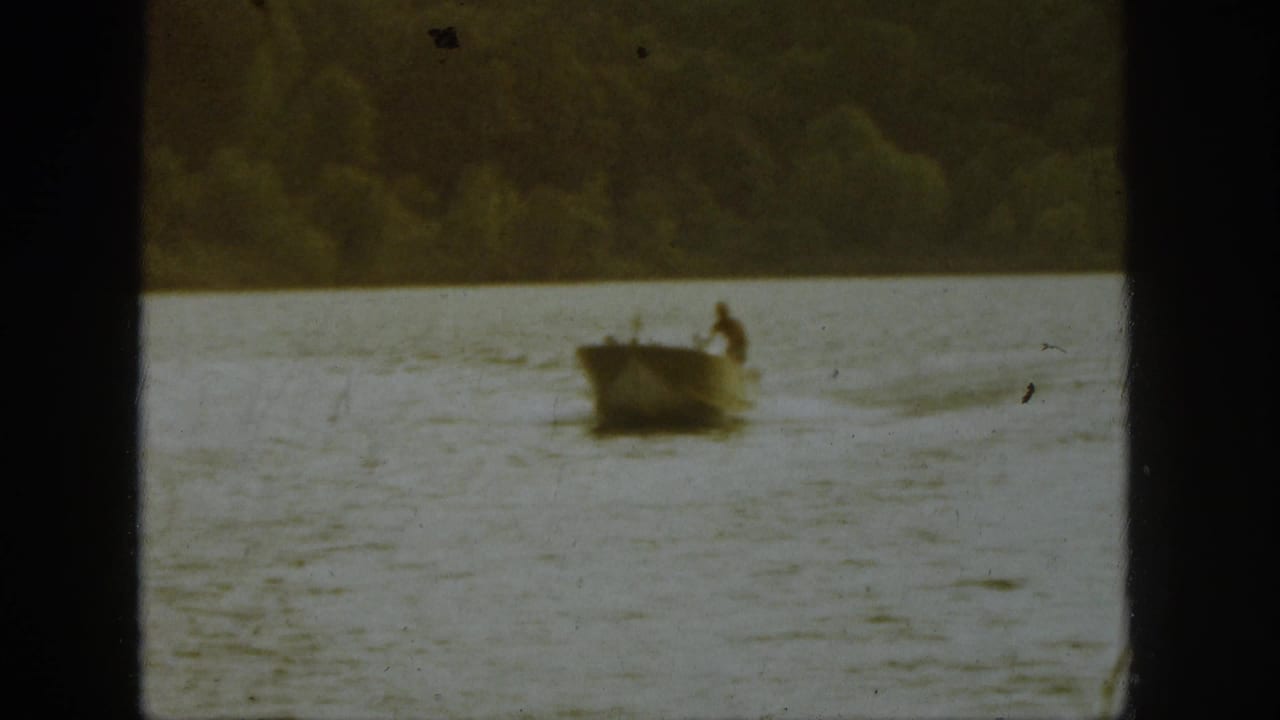 Small boat on a lake with a wooded shoreline in the distance.