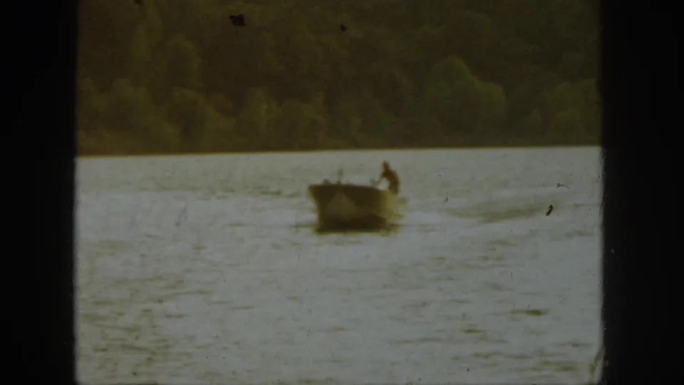 1961 Michigan 8mm frame showing a small boat on open lake water with a dark wooded shoreline beyond.