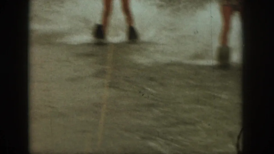 Home-movie frame from the Michigan lake scene showing lower legs in shallow water, likely moments before or after water-skiing activity.