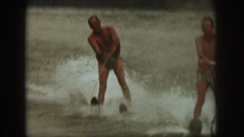 1961 Michigan home-movie frame showing a man in swim trunks holding a tow rope as water splashes around him on the lake.