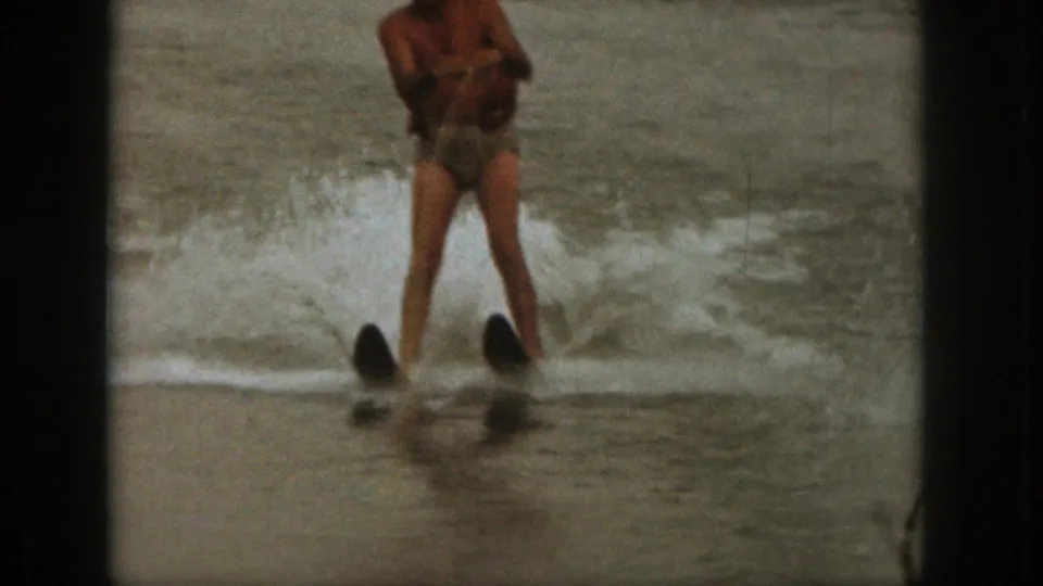 1961 Michigan lake footage shows an adult man water skiing toward the camera, with splashing water behind his skis.