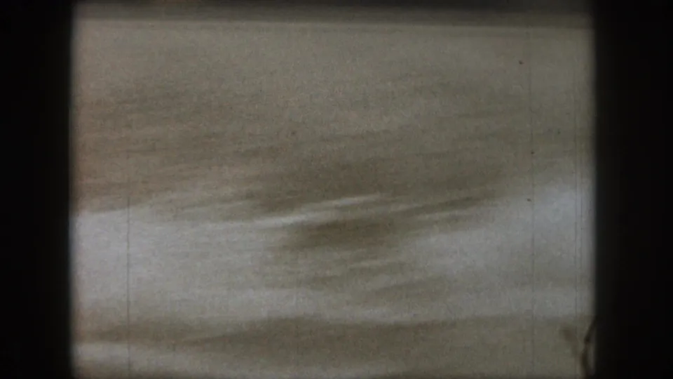 The frame holds mostly lake water and spray, with the skier out of view or indistinct in the soft 8mm scan.