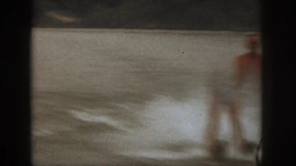A man in swim trunks is partly visible near the right edge of this 1961 Michigan lake recreation frame, with water and shoreline behind him.