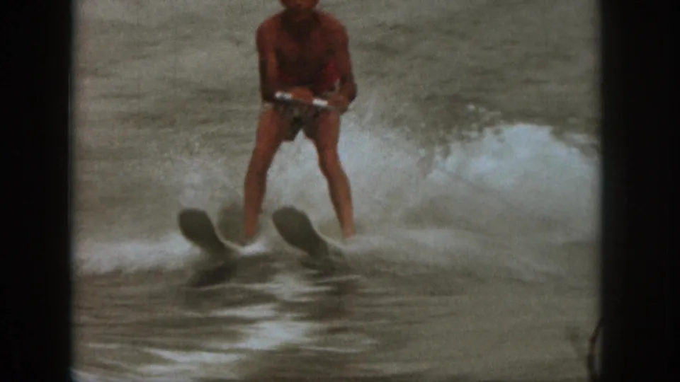 1961 Michigan 8mm frame showing the skier gripping a handle as twin skis cut through foamy lake water.