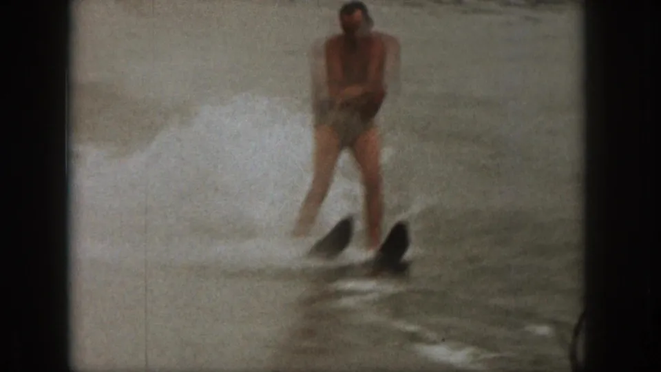 A man in swim trunks is pulled across a Michigan lake on water skis, with heavy spray behind him in 1961 8mm footage.