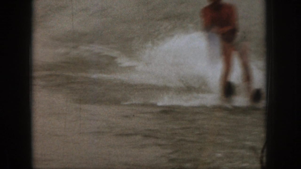 1961 Michigan 8mm frame showing a blurred man water skiing across a lake, with spray and dark film borders visible.