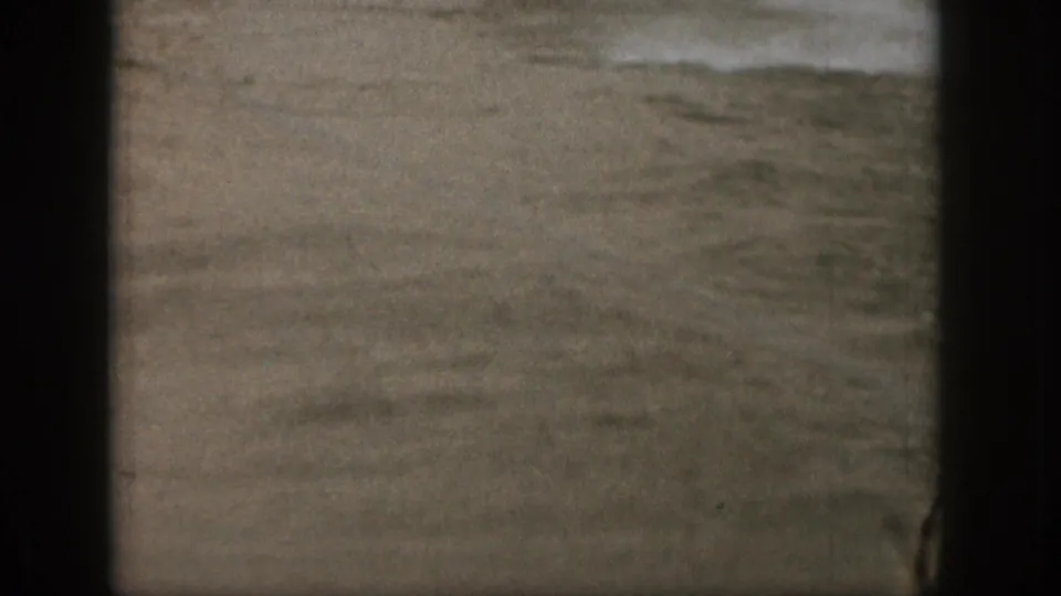 Soft 8mm frame showing lake water, faint spray, and a dark film or camera edge with no clear subject centered.