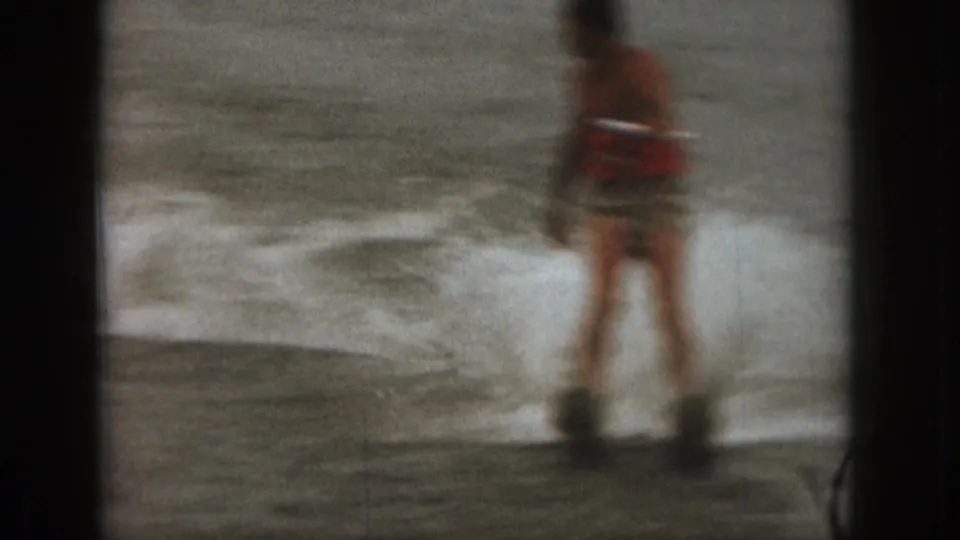 1961 Michigan 8mm frame showing a blurred rear view of a man water skiing away across the lake.