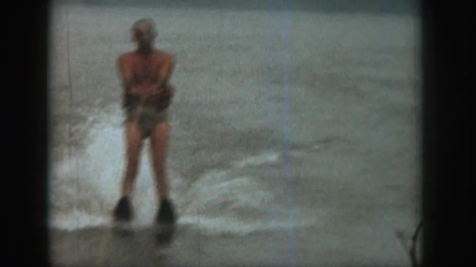 The final frame shows the adult skier from behind on a Michigan lake, moving away through a pale wake in 1961 home-movie footage.