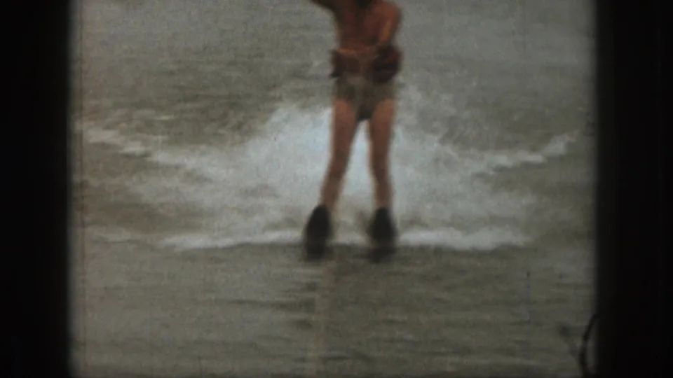 Adult man water skiing in the 1961 Michigan clip, partly cropped by the frame as lake spray rises behind him.