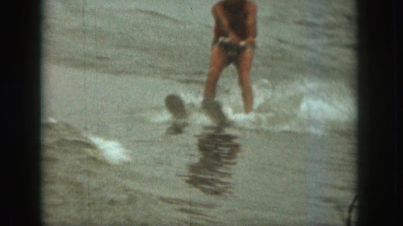1961 Michigan 8mm frame showing a shirtless adult water skier in swim trunks moving through spray on choppy water.