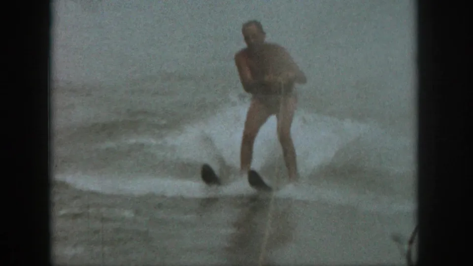 1961 Michigan 8mm frame showing the water skier leaning through spray on a lake, with soft grain and muted color.