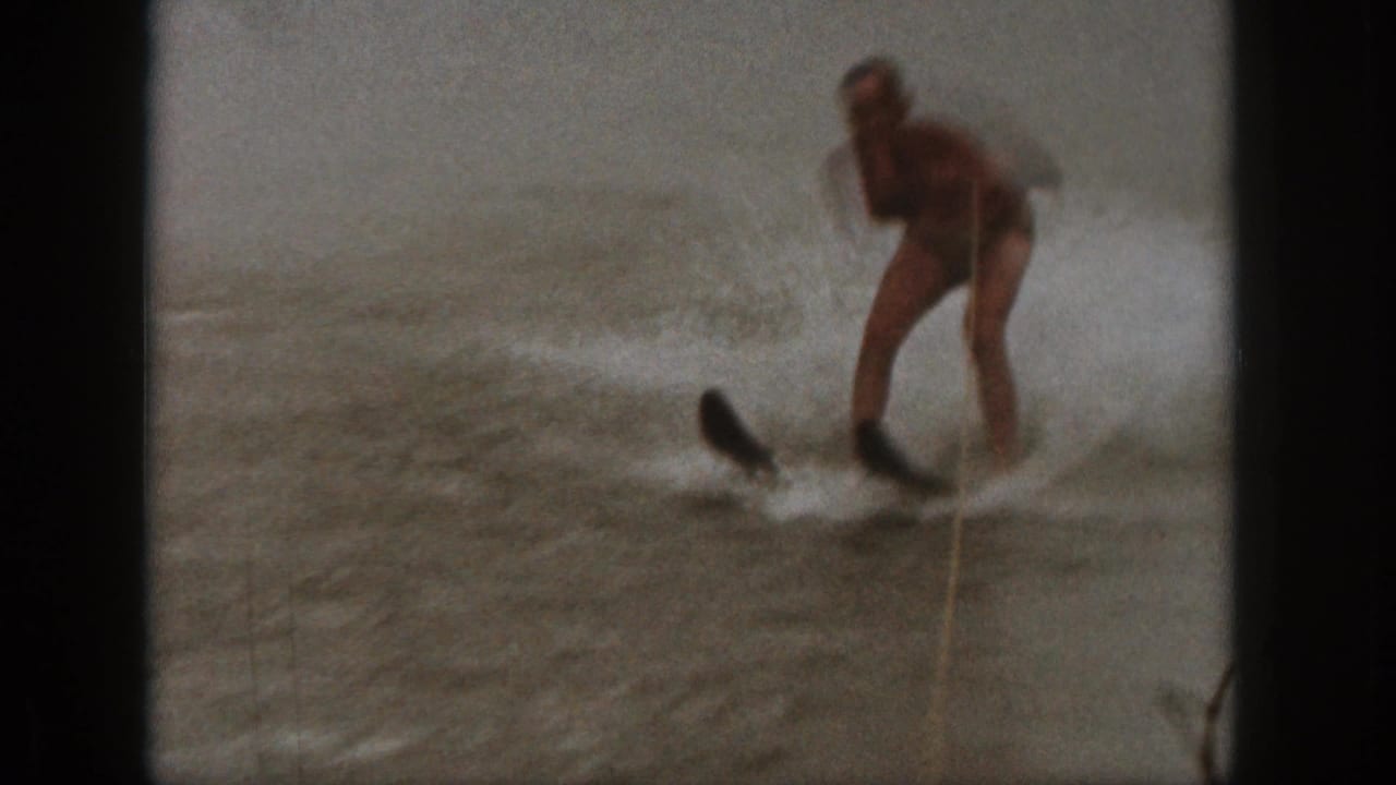 1961 Michigan 8mm frame of a water skier in a dark swimsuit gripping a tow rope as spray rises around the skis.