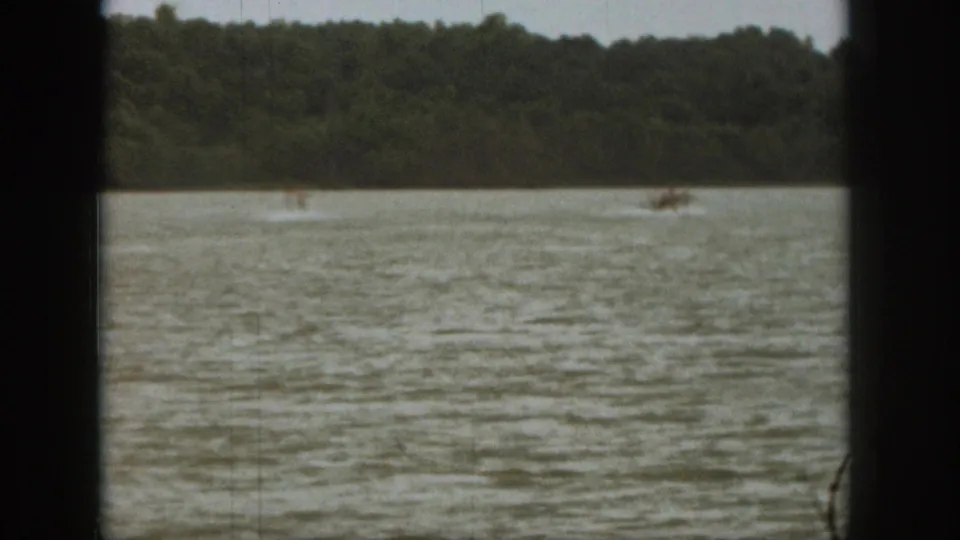 Wide 8mm view of Michigan lake recreation, with a small skier and boat wake set against a dark wooded shoreline.